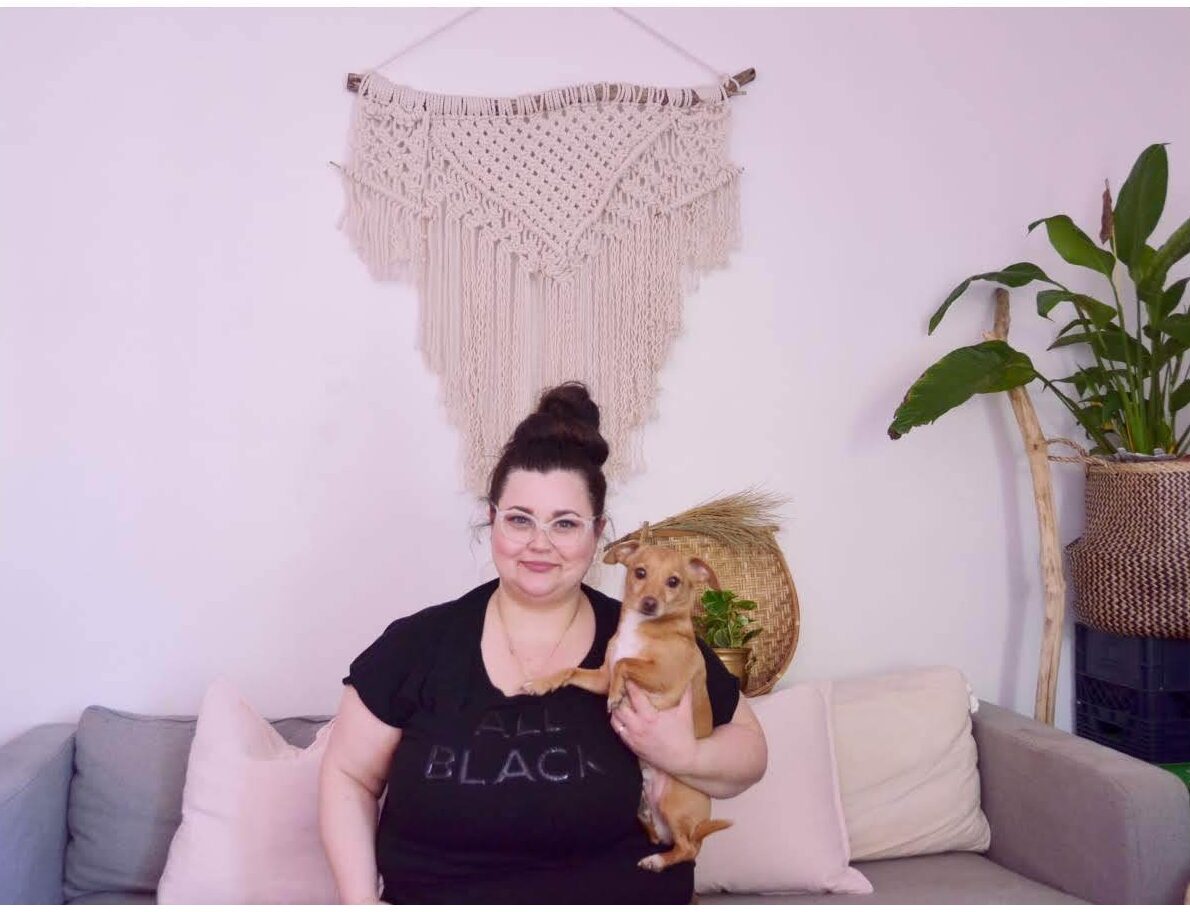 Alt-text for photo: Lina and her dog, a chiweenie, Buster, pose for a photo in a home setting with plants and macrame