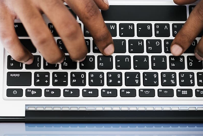 hands typing on a grey and black laptop keyboard