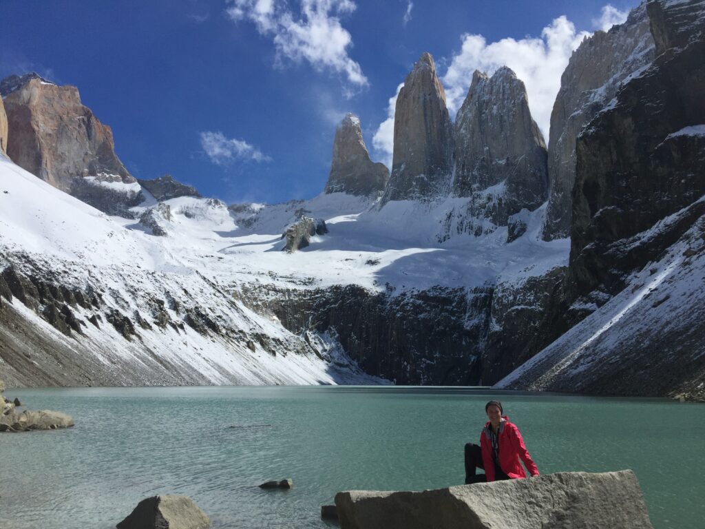 Isabella Peters sits atop a rock overlooking a beautiful glacial lake and snow-topped peaks at Torres del Paine National Park, Patagonia.