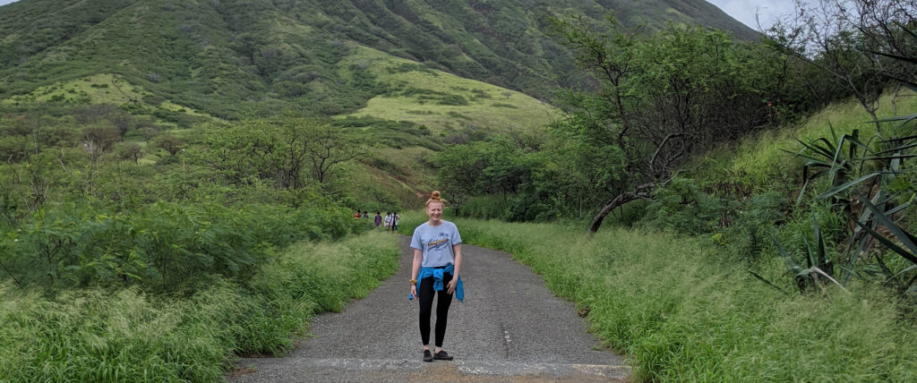 ScholCommLab member Isabelle Dorsch stands in the middle of a  gravel road, surrounded by greenery