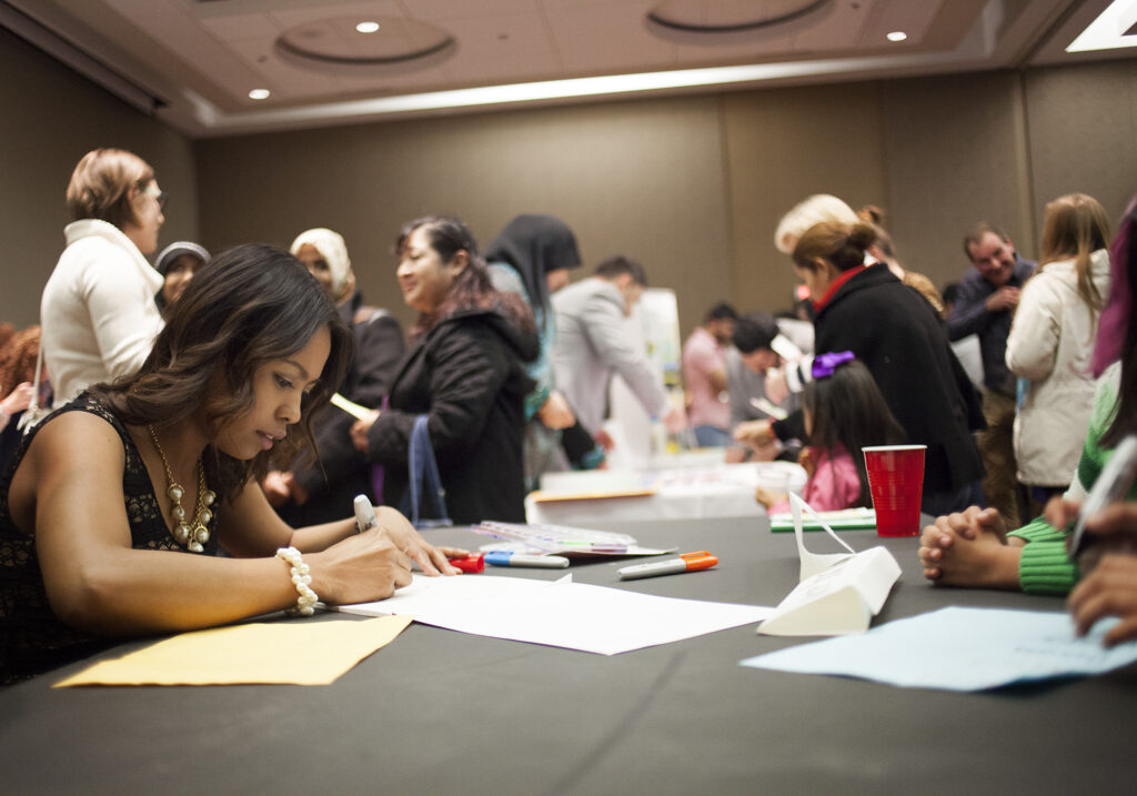 Photo of a room of people talking, writing, and learning. 