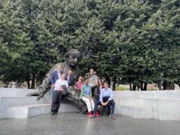 A group of people smile into the camera while seated at the Albert Einstein Memorial statue.