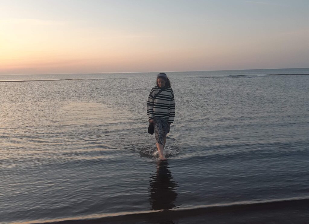 Maddie Hare, member of the Scholarly Communications Lab, wading along the shores of a New Brunswick beach at sunset
