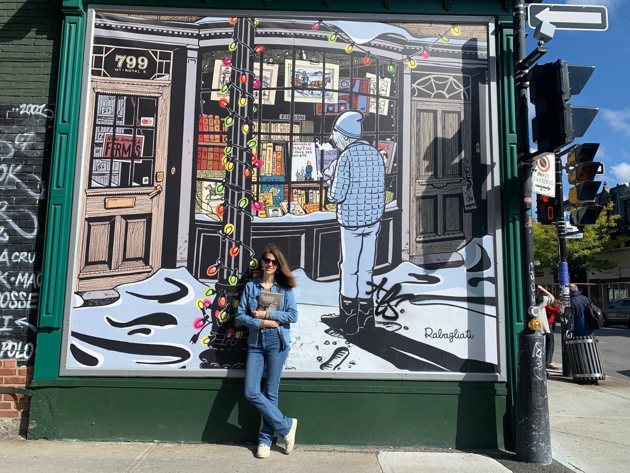 Lucía, research associate at the ScholCommLab, standing in front of a mural by Michel Rabagliati at Bouquinerie du Plateau in Montreal